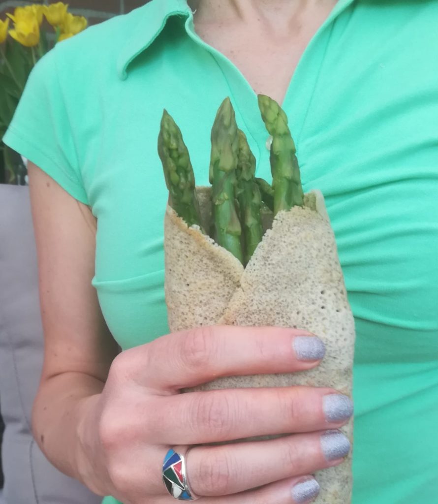 vrouw met in haar hand groene asperges in wrap/pannenkoek